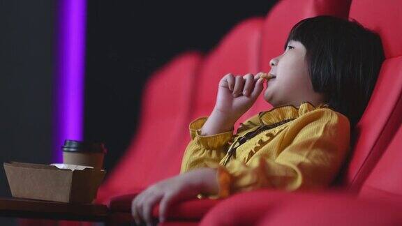 侧视亚洲中国年轻女孩一边吃薯条一边独自在电影院看电影