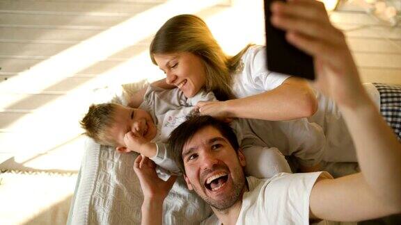 微笑的父母和宝宝在家里的床上自拍全家福