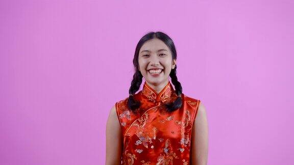 4K肖像亚洲女孩扎着辫子穿着红色的中国民族服装(旗袍)她在春节快乐地笑蓝色背景的孤立室内工作室
