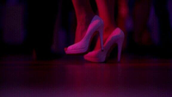 在夜总会或迪斯科舞厅的舞池上跳舞的女人和男人的脚的特写围观穿着高跟鞋的美腿女人跳舞