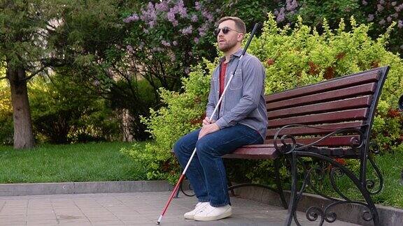 一个盲人拄着拐杖坐在公园的长凳上