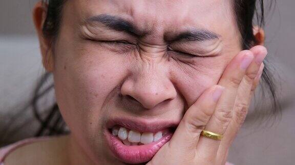 亚洲女子用手托着他的脸颊患有牙痛、蛀牙、牙齿敏感、蛀牙健康和牙科保健