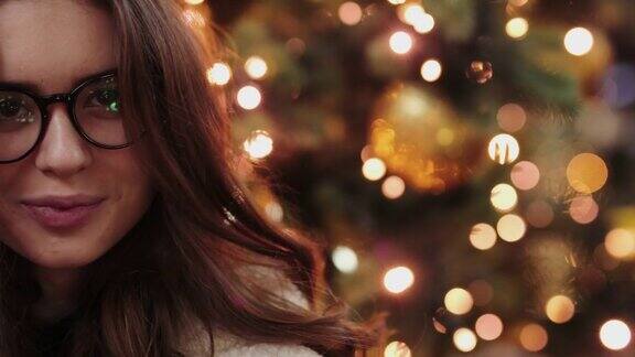 漂亮的女孩戴着鹿角和眼镜给相机一个吻并微笑圣诞灯的背景