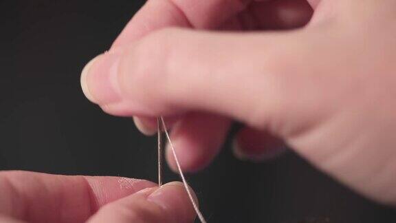一个裁缝的手插入一根线进针眼的特写在家修理衣服