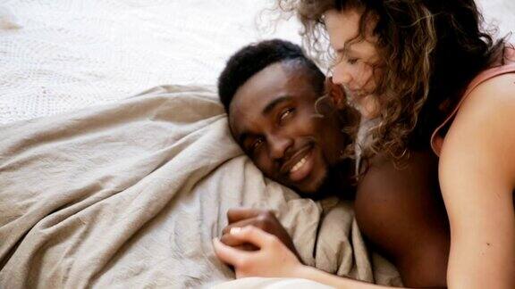 多民族情侣浪漫的早晨女人躺在男人身上在床上拥抱着男人和女人说话手牵手