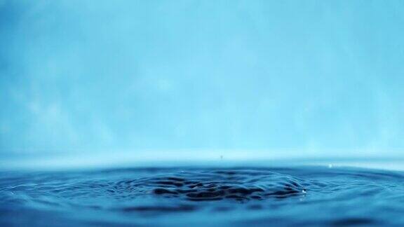 慢动作视频的水面与下落的水滴在一个蓝色的背景泼水