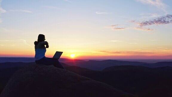 日落时分在山顶上工作的自由职业女性疲惫地举起双手合上笔记本电脑