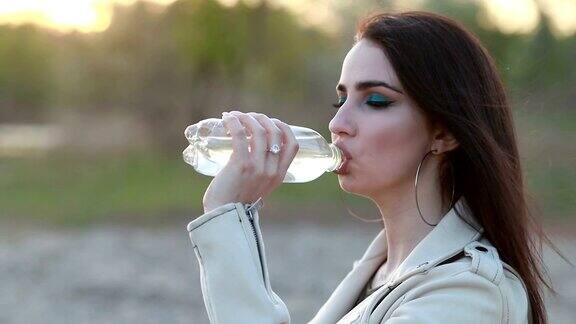 年轻女子在日落时喝水女孩喝瓶子里的水
