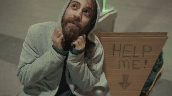 面对夜晚街上孤独寒冷的流浪汉他旁边的纸板上写着“帮助我”无家可归慢镜头4k