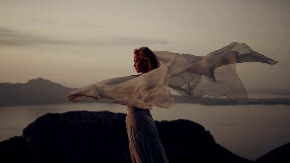 浪漫的女孩穿着长裙享受着风站在悬崖上