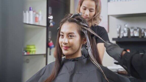 年轻的亚洲美丽的女孩在沙龙改变发型和颜色美发师在美容院给一位女士染发女人笑着看着镜子美发美容沙龙概念