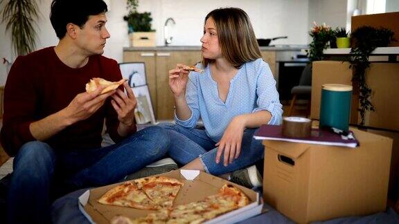 一对年轻夫妇坐在床垫上吃披萨当晚餐