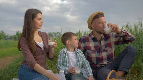 家庭野餐快乐的年轻夫妇和孩子男孩喝牛奶同时放松在野外的自然