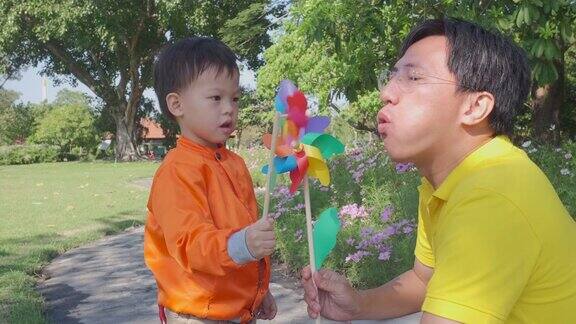 亚洲父亲有乐趣与他的孩子吹风车玩具爸爸和儿子花优质时间玩在夏季的自然