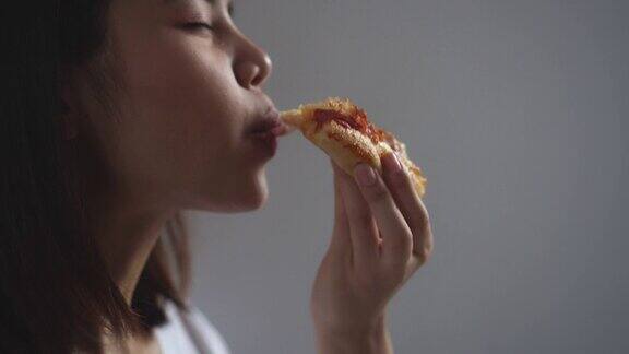 年轻的亚洲女人在家里吃着美味的披萨