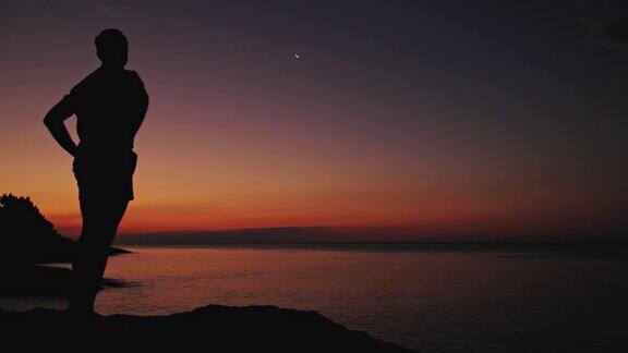 一个人的剪影看着月亮和星星在海上的地平线
