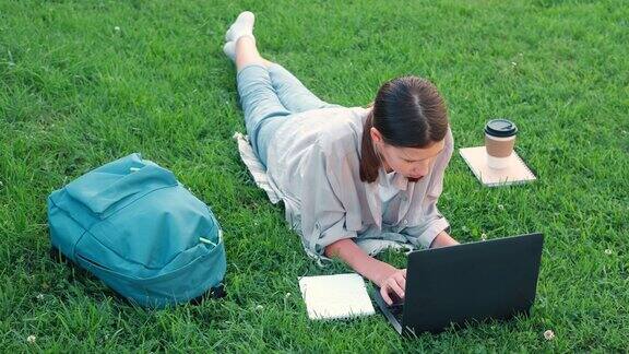 女学生躺在草地上使用笔记本电脑远程学习