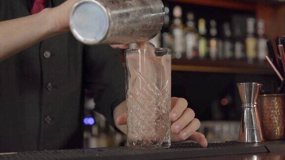调酒师将蜜桃色的鸡尾酒从摇酒器倒入盛满冰块的玻璃杯中
