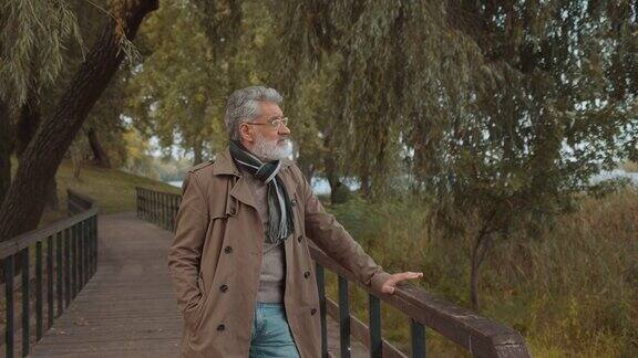 白发苍苍的老人站在公园的桥上欣赏着森林的景色