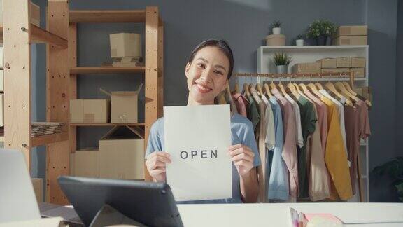 开朗迷人的年轻亚洲女士带着随意的微笑在她的服装店展示开放的标志从新冠状病毒大流行重新开放新冠肺炎疫情后重新开业小企业主兴奋不已