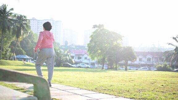 一位华裔老年妇女在公园晨练在人行道上跑步