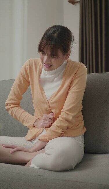 年轻的亚洲女性胃痛得厉害一个女人因为胃痛坐在家里的沙发上