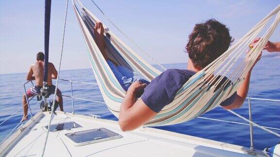 在吊床上放松的男人在阳光明媚的帆船上喝啤酒实时的