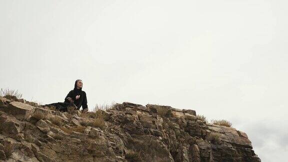 一个穿着黑衣服的女人坐在山顶的悬崖边上大的湖