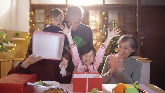 多代家庭坐着吃健康食品同时打开圣诞礼物礼盒在家