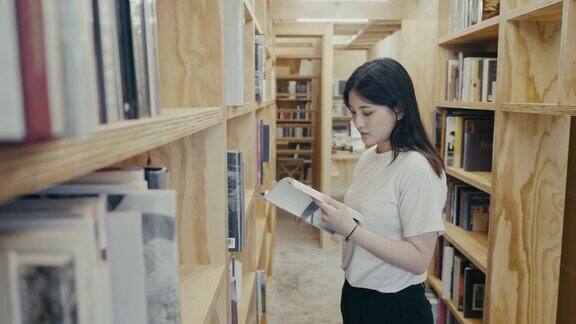 年轻的亚洲大学生在图书馆里找书(慢镜头)