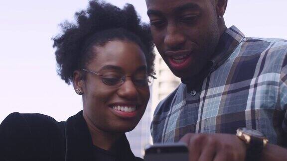 一对非洲裔美国夫妇在户外看着手机上的照片笑着