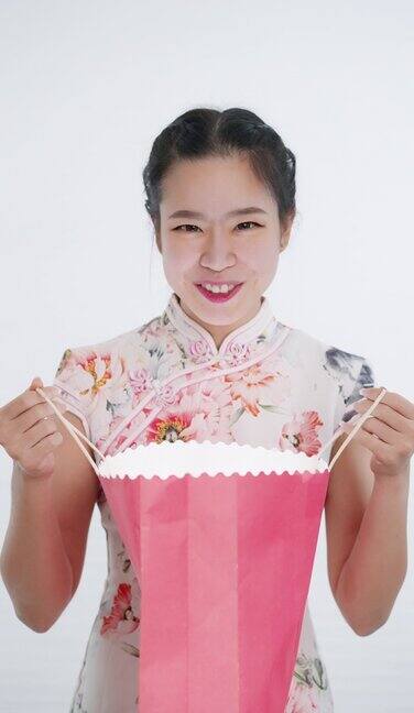 中国亚洲妇女在春节期间打开粉红色的购物袋在白色的背景下穿着旗袍白色花卉图案的衣服遇到了一个惊喜