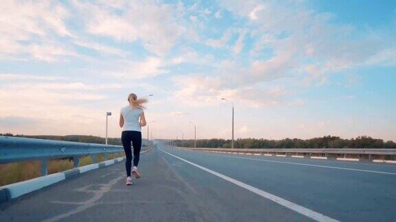 一个穿着白色t恤穿着鲜艳运动鞋留着长发的运动型女孩在城外的一条空旷的小路上奔跑国家体育比赛日落前美丽的天空