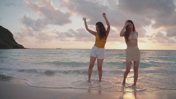 两个亚洲年轻女子在海滩上跳舞享受乐趣