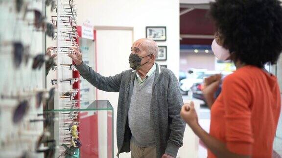 一位年轻的女售货员在眼镜店帮助一位高级顾客购买眼镜两人都戴着面罩