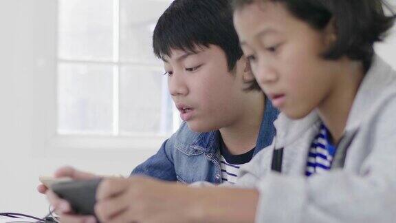 近距离的亚洲可爱的女孩和年轻的男孩玩在智能手机和平板电脑上的竞争视频游戏在横向横向模式中持有他们60帧秒摄影