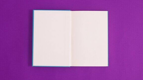 蓝色古董精装书出现和打开与副本空间在紫色的背景停止运动平铺