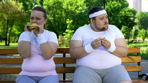 肥胖的年轻夫妇吃汉堡沉迷于垃圾食品缺乏意志力