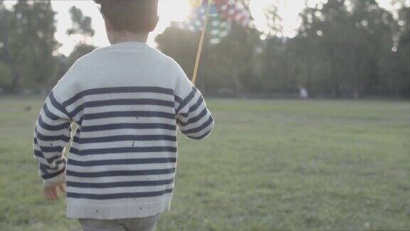 小男孩拿着纸扇在草坪上奔跑的背影