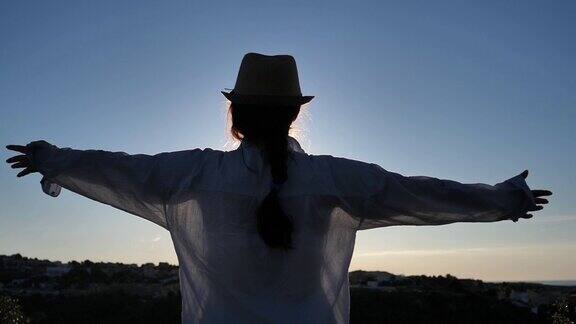 女孩站在山顶看着城市和大海在日落的时候举起她的手向太阳