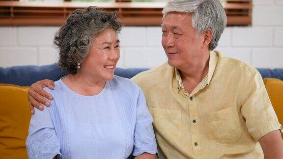 一对亚洲老夫妇坐在家里的沙发上看着镜头微笑