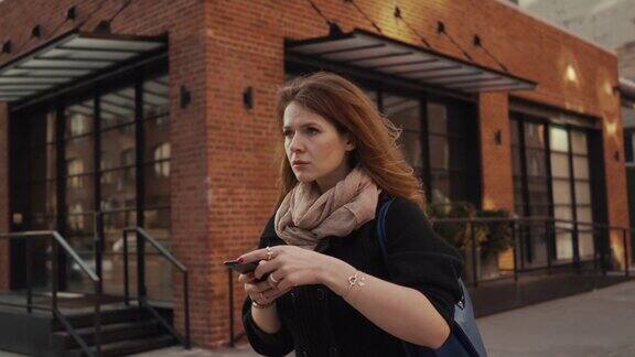 美丽的红发女孩在大城市匆忙使用智能手机等待一个朋友还是失去了