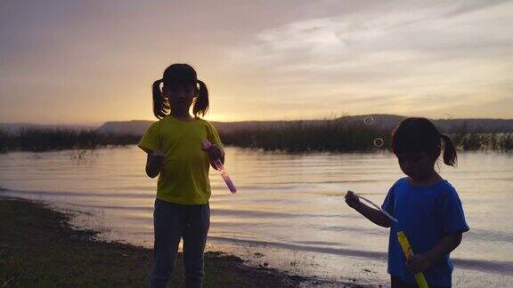 日落时分两个孩子在湖边玩泡泡