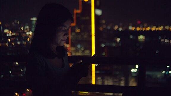 年轻的亚洲女人在晚上的城市里用美丽的散景用智能手机