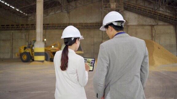 年轻的亚洲企业参观大型工厂用平板电脑谈生意