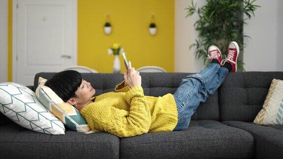 年轻的中国女子躺在家里的沙发上用智能手机