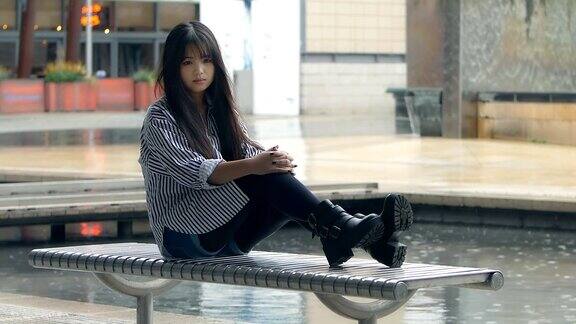 年轻的中国女人坐在长椅上等人:悲伤的女人