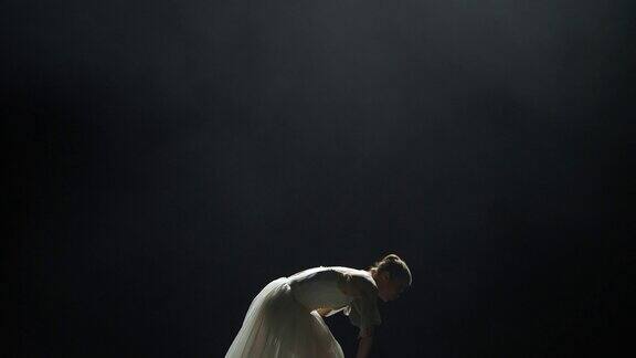 戏剧性的舞蹈优雅的女人穿着白色的芭蕾舞裙在黑色的背景上表演舞蹈元素在黑暗的舞台上使用镁砂薄雾效果慢动作