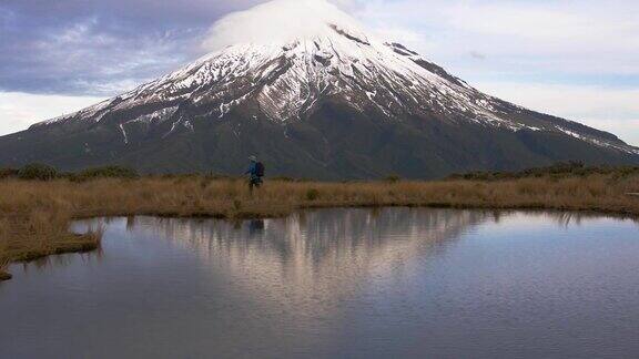 慢动作-旅行者步行横向观看塔拉纳基火山在北岛的新西兰和反射山和登山者在湖中新西兰被