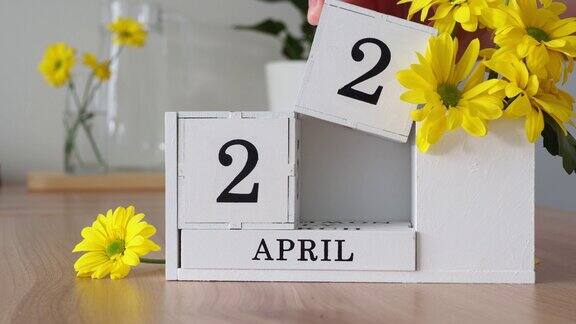 春月四月二十二日一个女人的手翻动着一本立体日历白色的万年历在黄花旁边的桌子上一个月后更改日期每个月的每一天数量